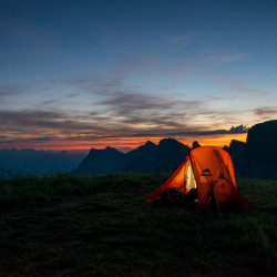 Oranges Zelt vor Bergsilhouetten in der Dämmerung, Biwak am Chäserrugg