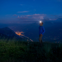 Person mit Stirnlampe über den Lichtern im Tal, Biwak am Chäserrugg