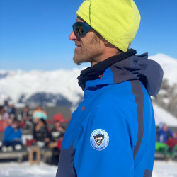 Snowboardlehrer mit gelber Mütze und blauer Jacke, Der Snowboarder
