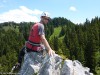 Kletterer mit Helm auf einem Felsgrat über dem Wald