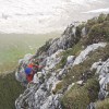Kletterer in roter Jacke an einem grasigen Grat, Alpstein