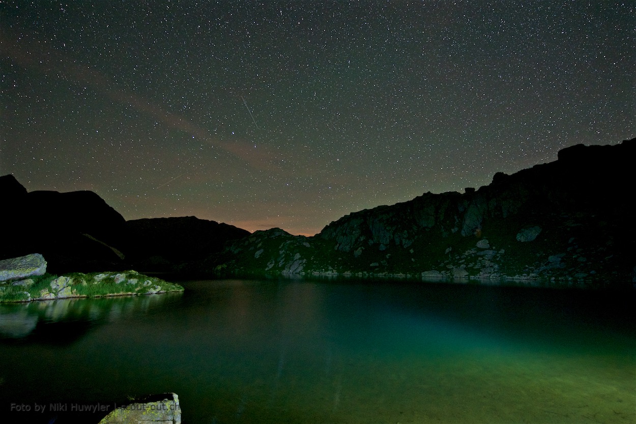 Nacht der Perseiden: Grünlich beleuchteter Bergsee bei Nacht