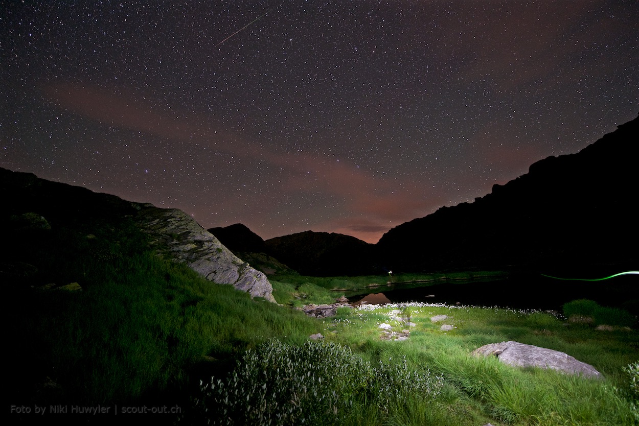 Nacht der Perseiden: Beleuchtete Wiese und Felsen unter dem Sternenhimmel