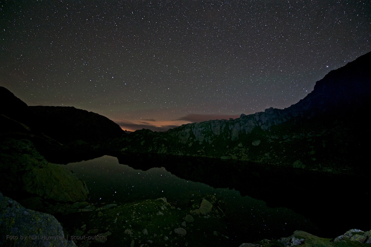 Nacht der Perseiden: Bergsee mit Restlicht am Horizont und Sternen