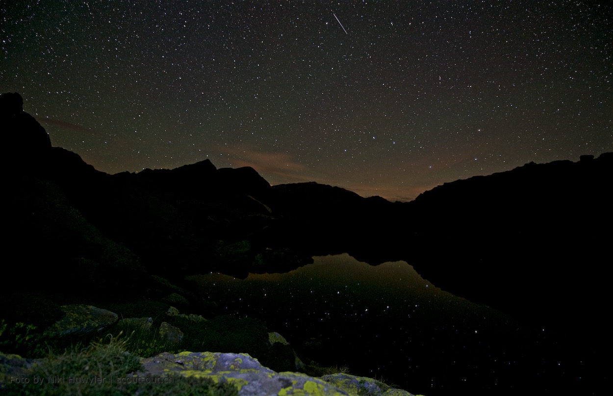 Nacht der Perseiden: Sternenhimmel über einem Bergsee mit Felsen