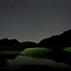 Nacht der Perseiden: Beleuchtetes Wollgras an einem Bergsee bei Nacht