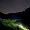 Nacht der Perseiden: Lichtkegel einer Stirnlampe am Seeufer unter Sternen