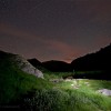 Nacht der Perseiden: Beleuchtete Wiese und Felsen unter dem Sternenhimmel