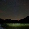 Nacht der Perseiden: Beleuchtete Felsen am See unter Sternen