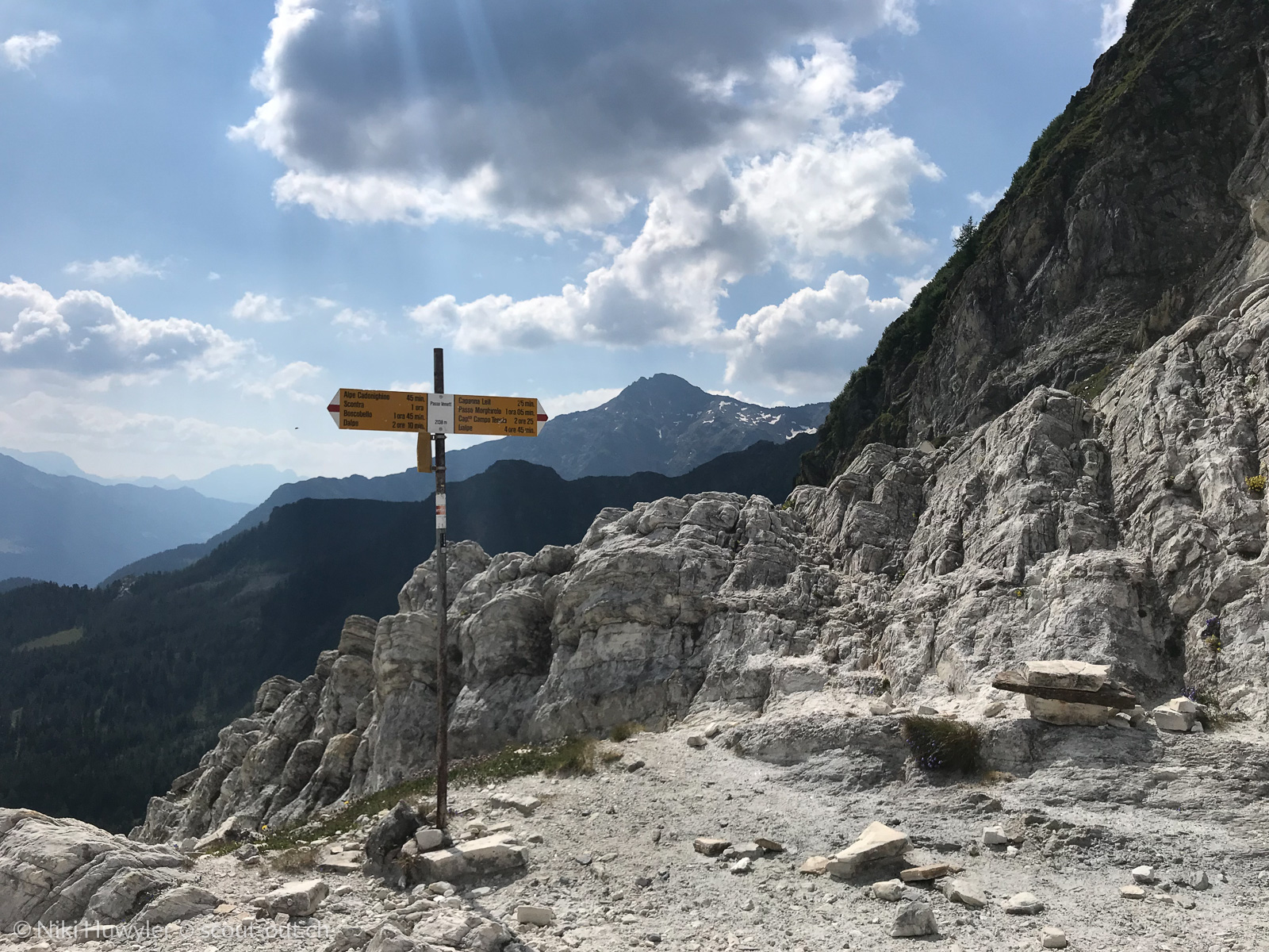 Wegweiser auf einem Geröllpfad unter Felswänden, Via Alta della Verzasca